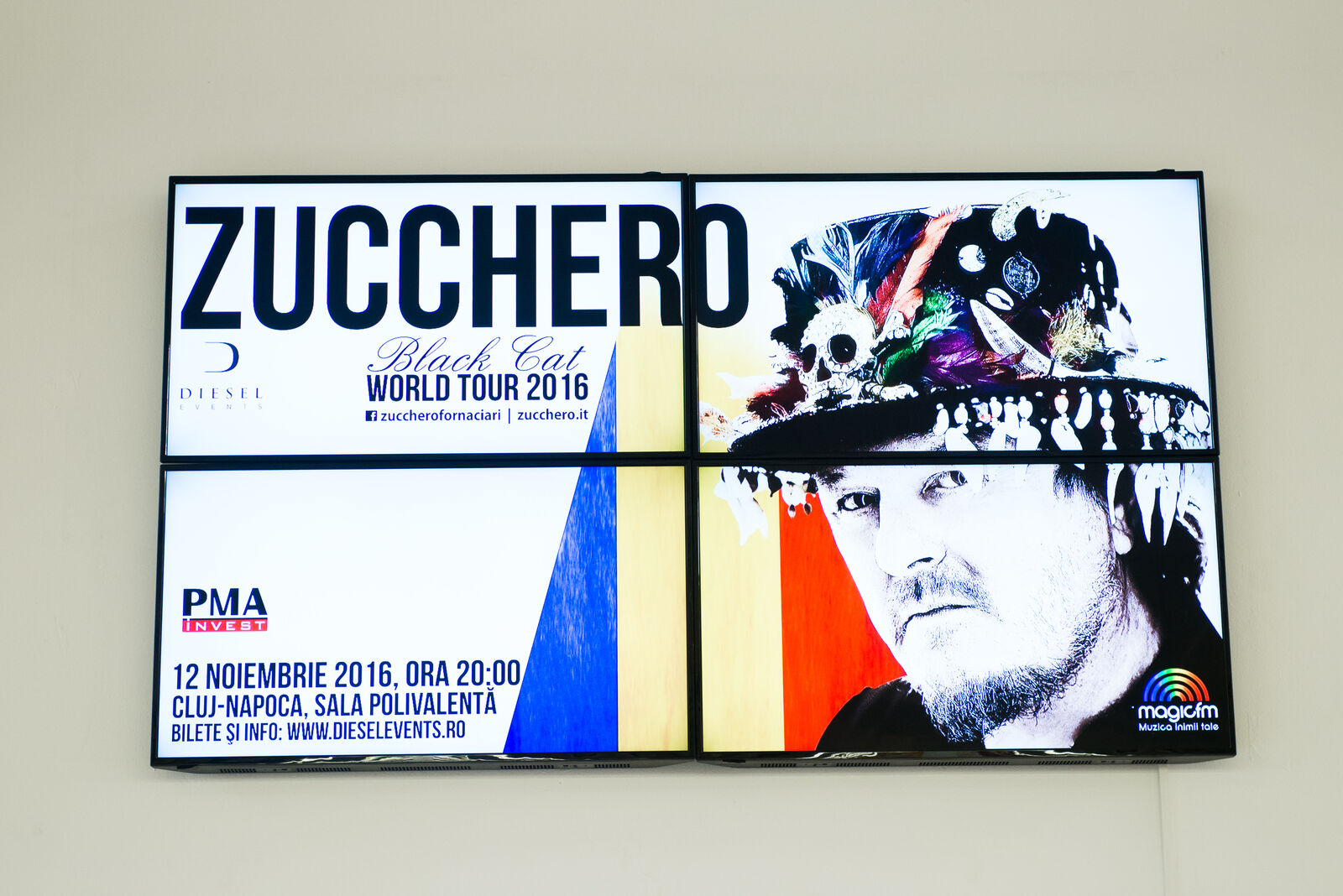 Four synced panels form one seamless video wall showing a high-contrast concert campaign in a mall foyer.