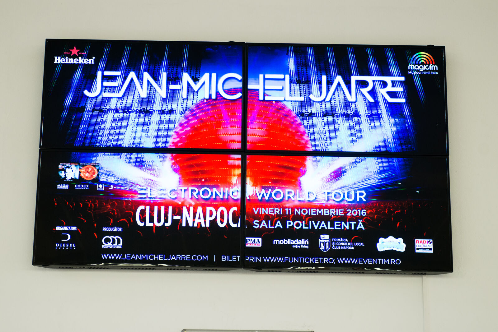 A 2 by 2 video wall in a mall foyer runs one full-bleed event promo across four tiled panels as a single image.