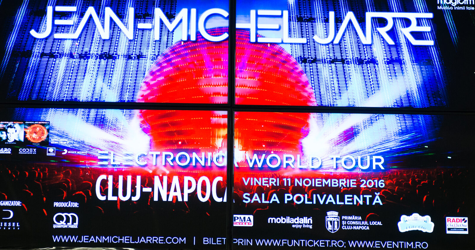 A 2 by 2 video wall in a shopping-mall foyer runs one full-bleed event promo across four tiled panels.