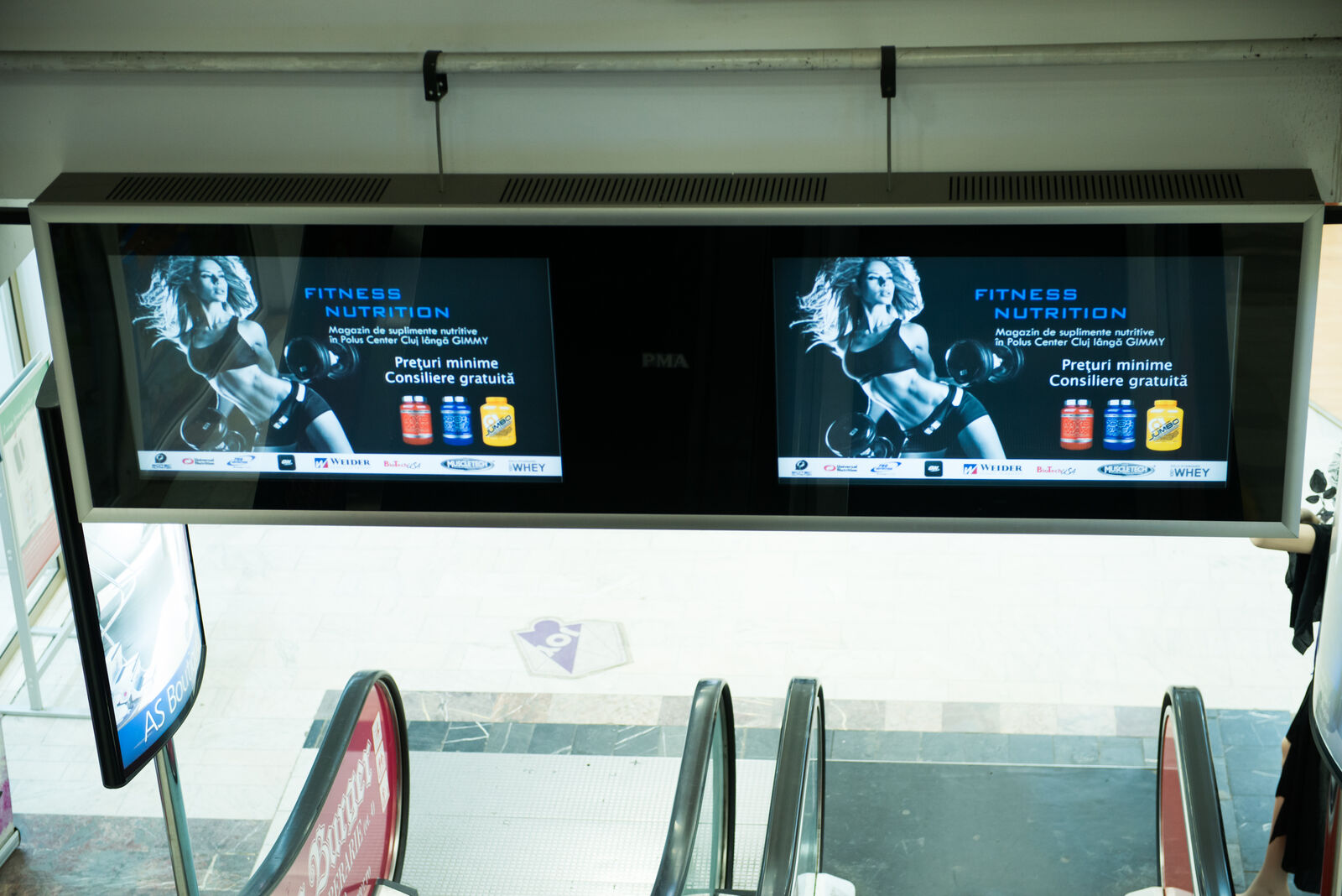 A close view of the dual screens at the top of a mall escalator showing crisp, legible advertising.