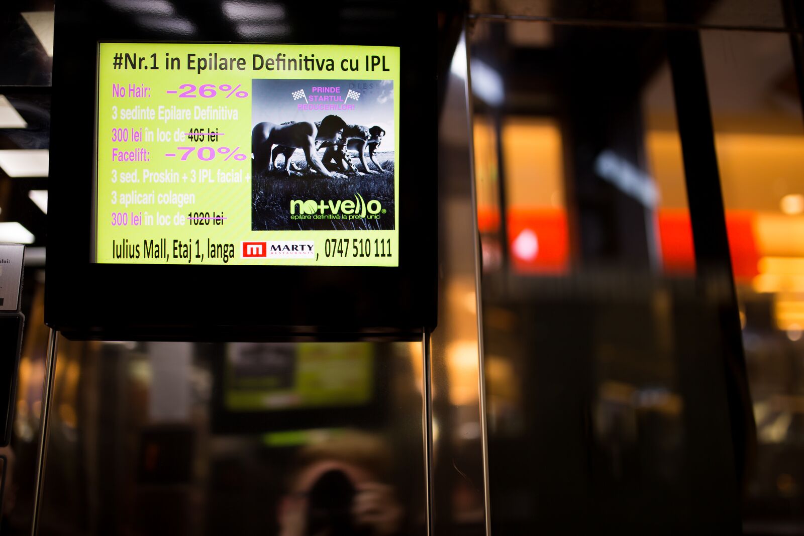 A free-standing bright screen in an empty mall corridor at night, showing a beauty-clinic offer.