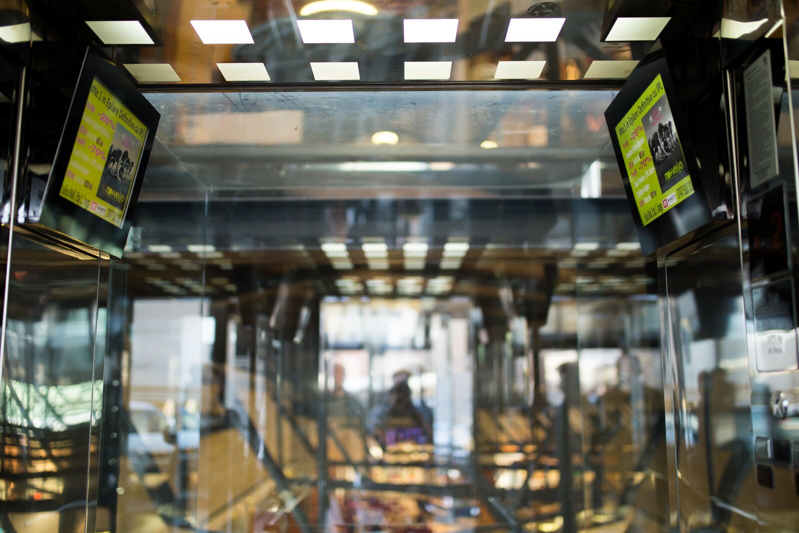 Two screens on opposite sides of a glass lift shaft, both playing the same promotional content.